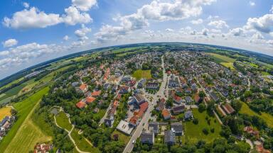 Vista aérea de uma cidade com uma rua central, campos verdes ao redor e casas espalhadas.