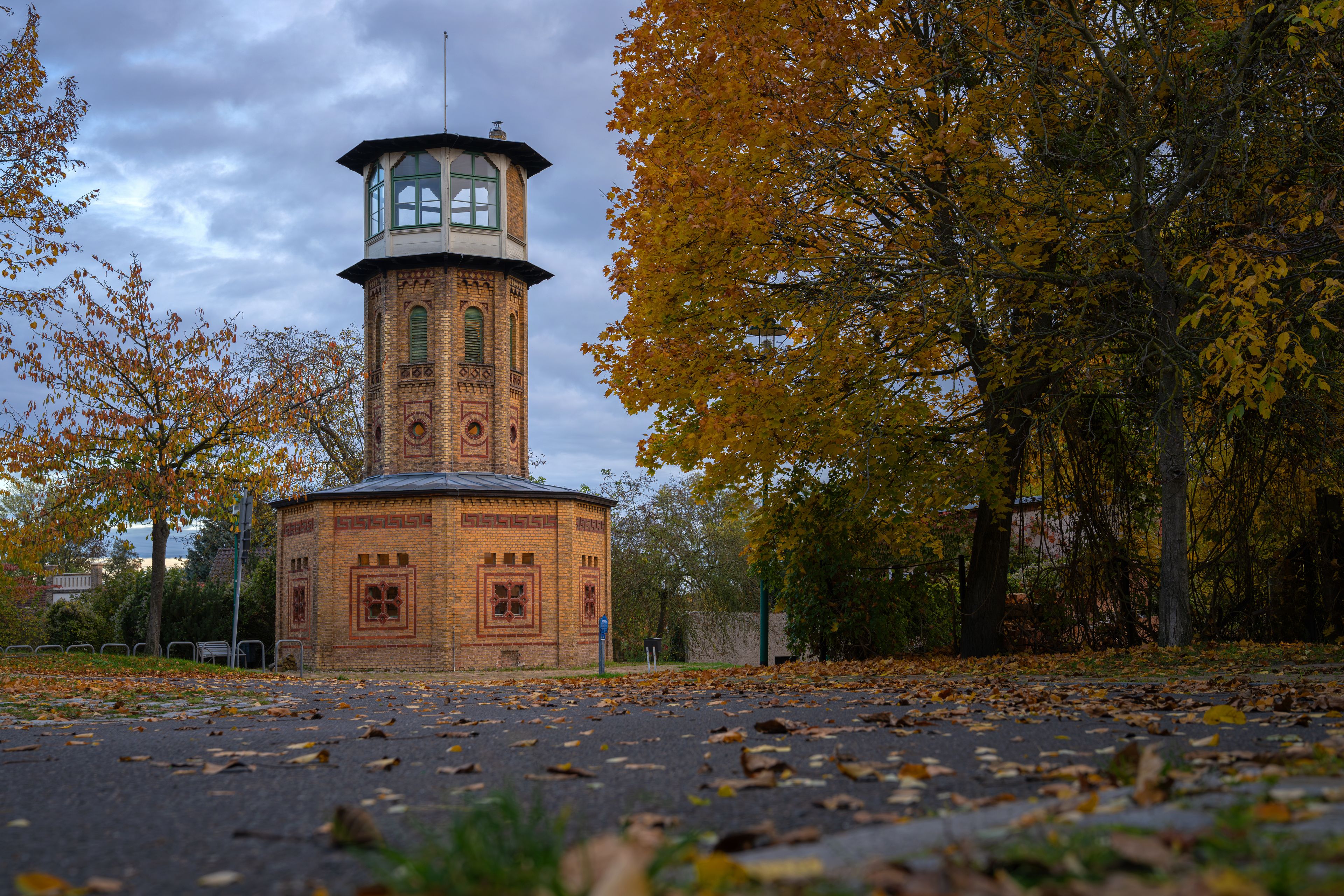 A brick tower with a clock, surrounded by autumn trees and fallen leaves.