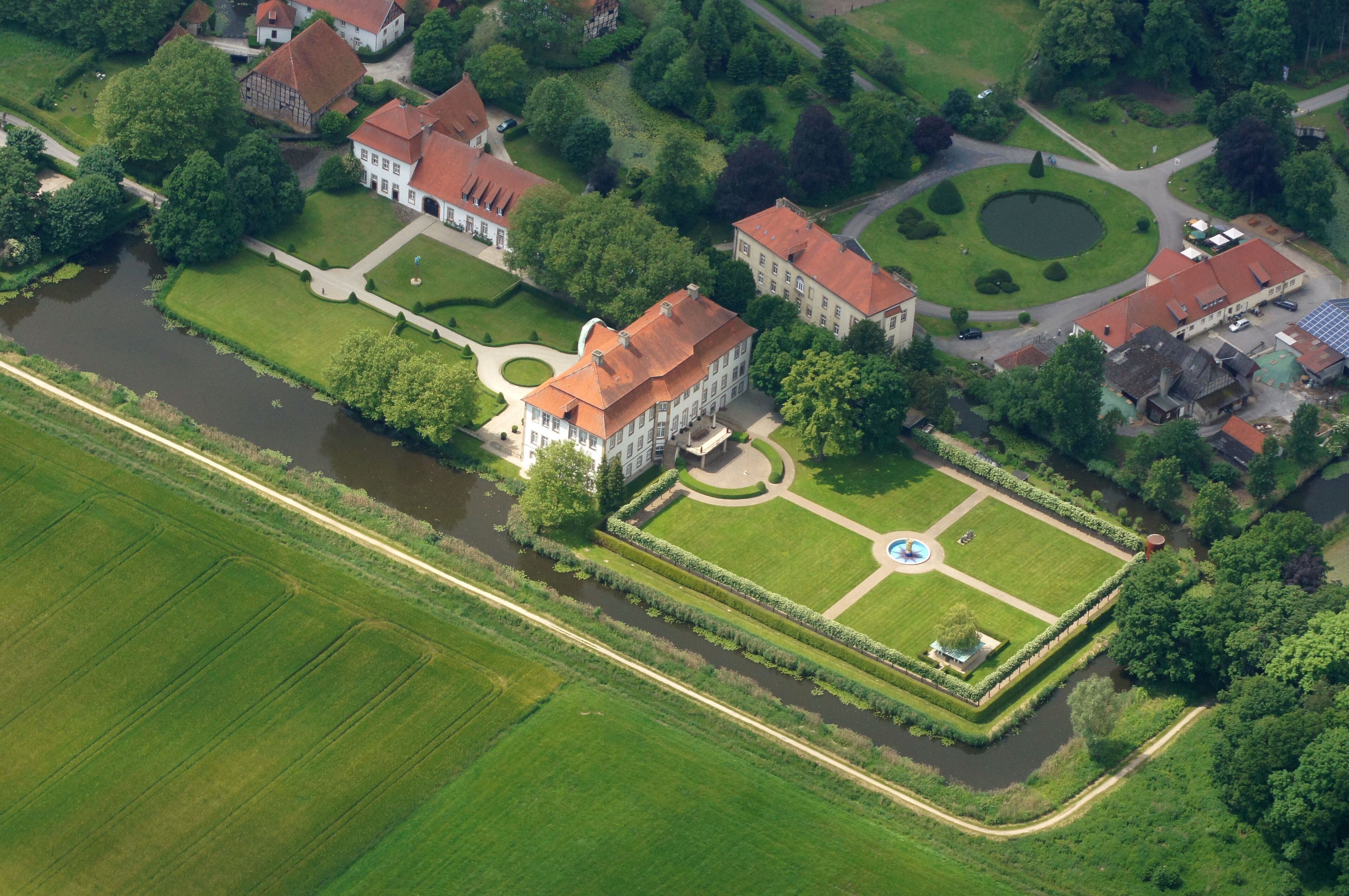 An aerial view of a large estate with multiple buildings, a circular pond, and well-maintained gardens.