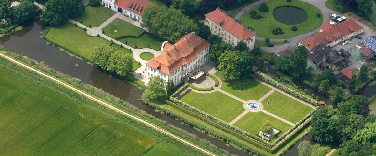 An aerial view of a large estate with multiple buildings, a circular pond, and well-maintained gardens.