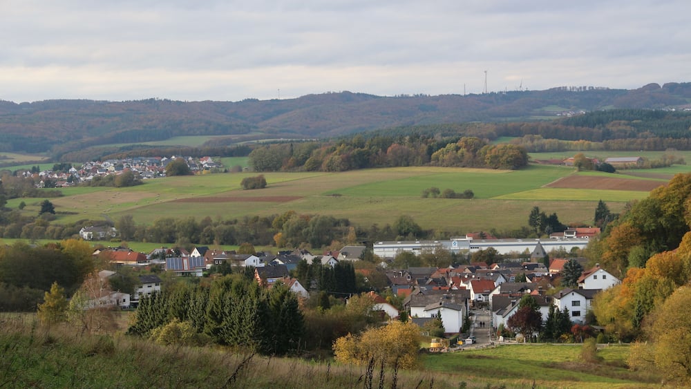 A rural landscape with a village, rolling hills, and a bridge.