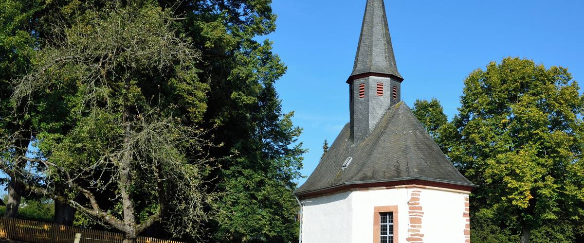 A small church with a pointed steeple and a wooden fence in the foreground.