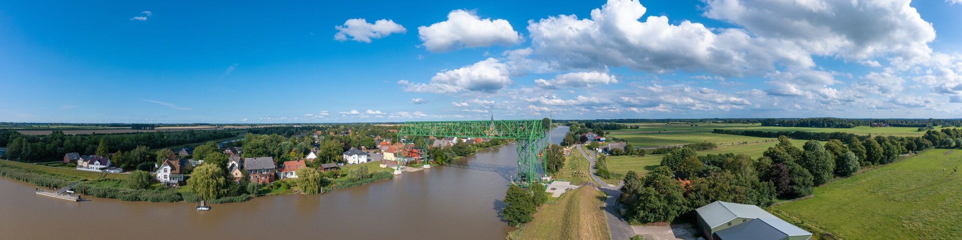 Un río con un puente, casas y campos.