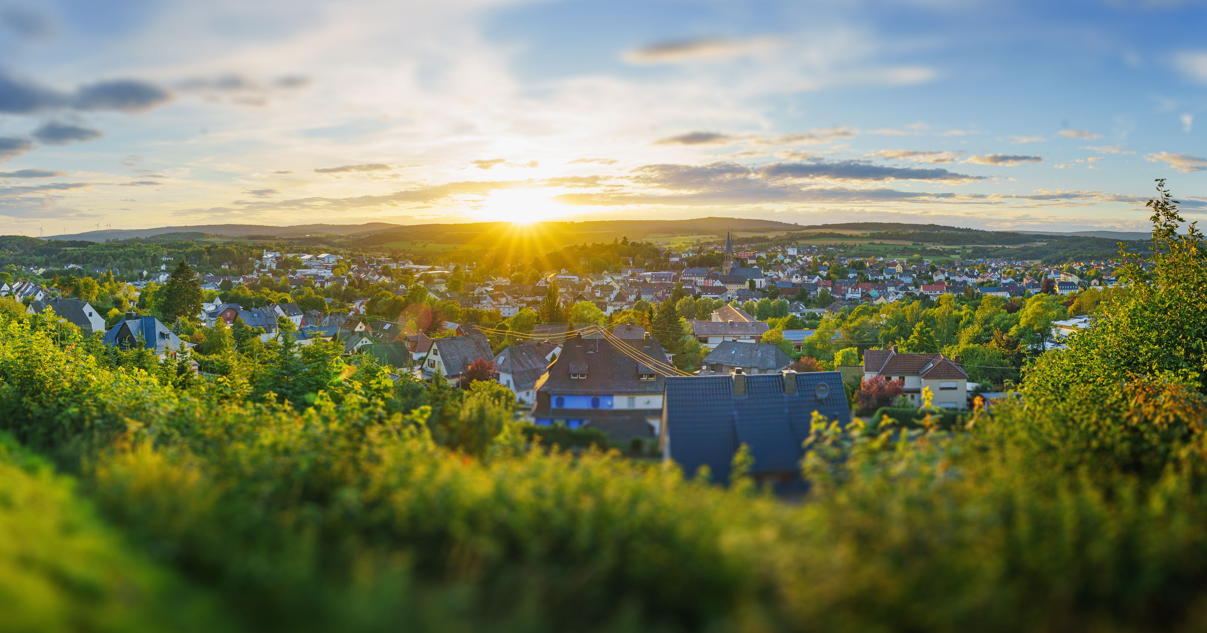 A town at sunset with a church spire, houses, and wind turbines in the distance.