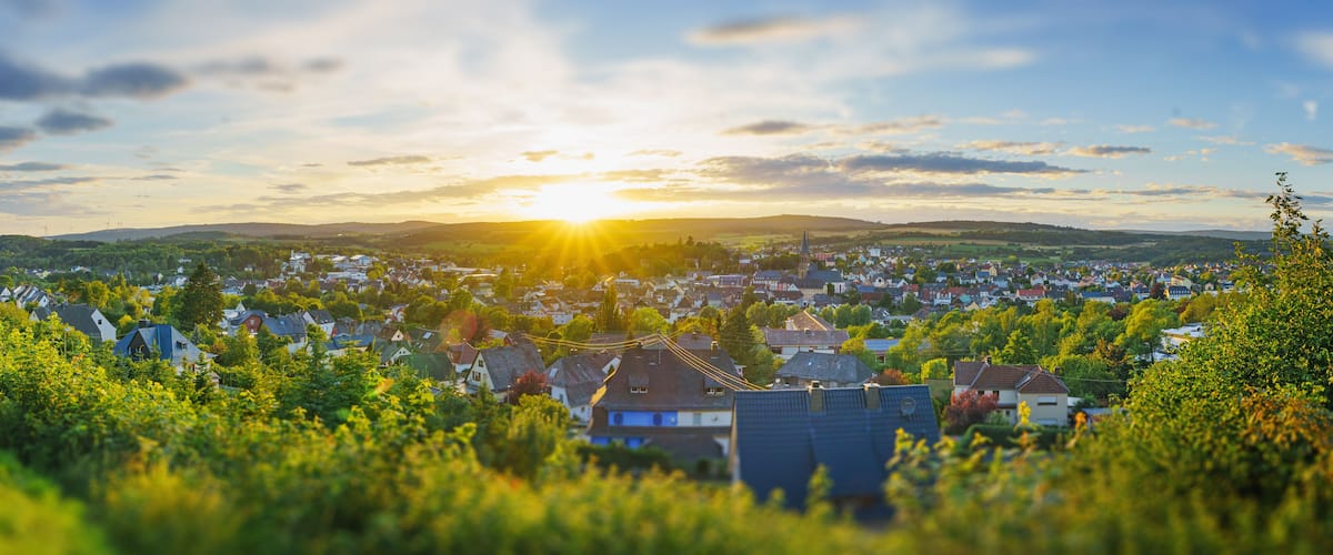 A town at sunset with a church spire, houses, and wind turbines in the distance.