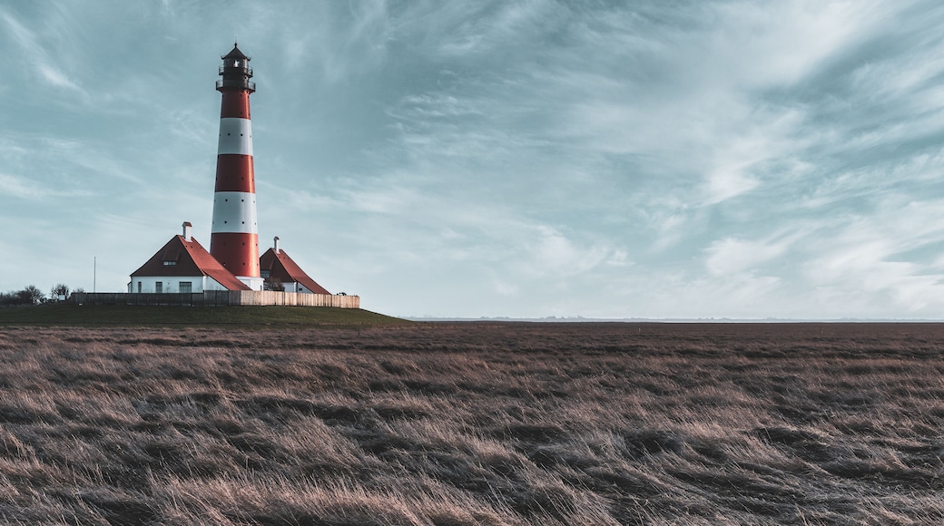 A red and white lighthouse with a white building nearby, set against a cloudy sky over a grassy field.