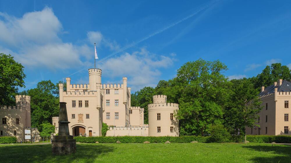 A castle with multiple towers, surrounded by lush green trees and a clear blue sky.