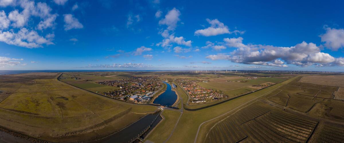 An aerial view of a town with a river, fields, and wind turbines in the distance.