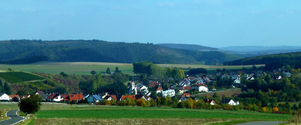 A rural village nestled in a valley with rolling hills and vineyards in the background.