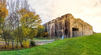 A large rock formation with a viewing platform, surrounded by grassy fields and trees.