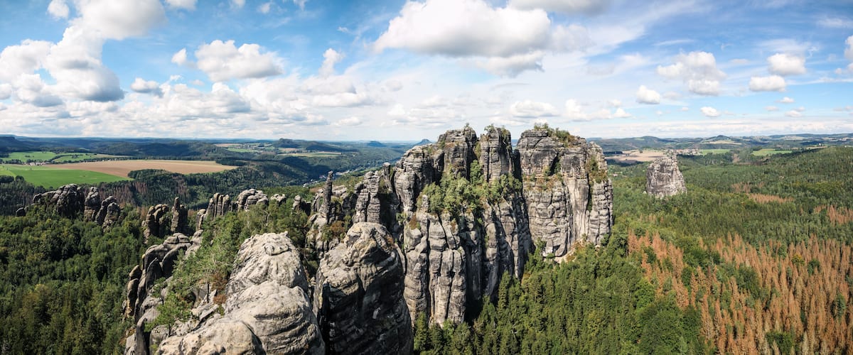 A landscape with prominent rock formations, dense forests, and a distant view of rolling hills and fields.