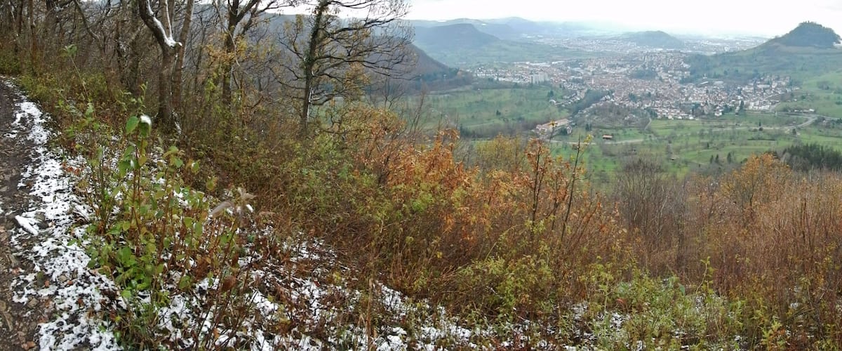 A mountainous landscape with a town in the valley, autumn foliage, and snow patches.