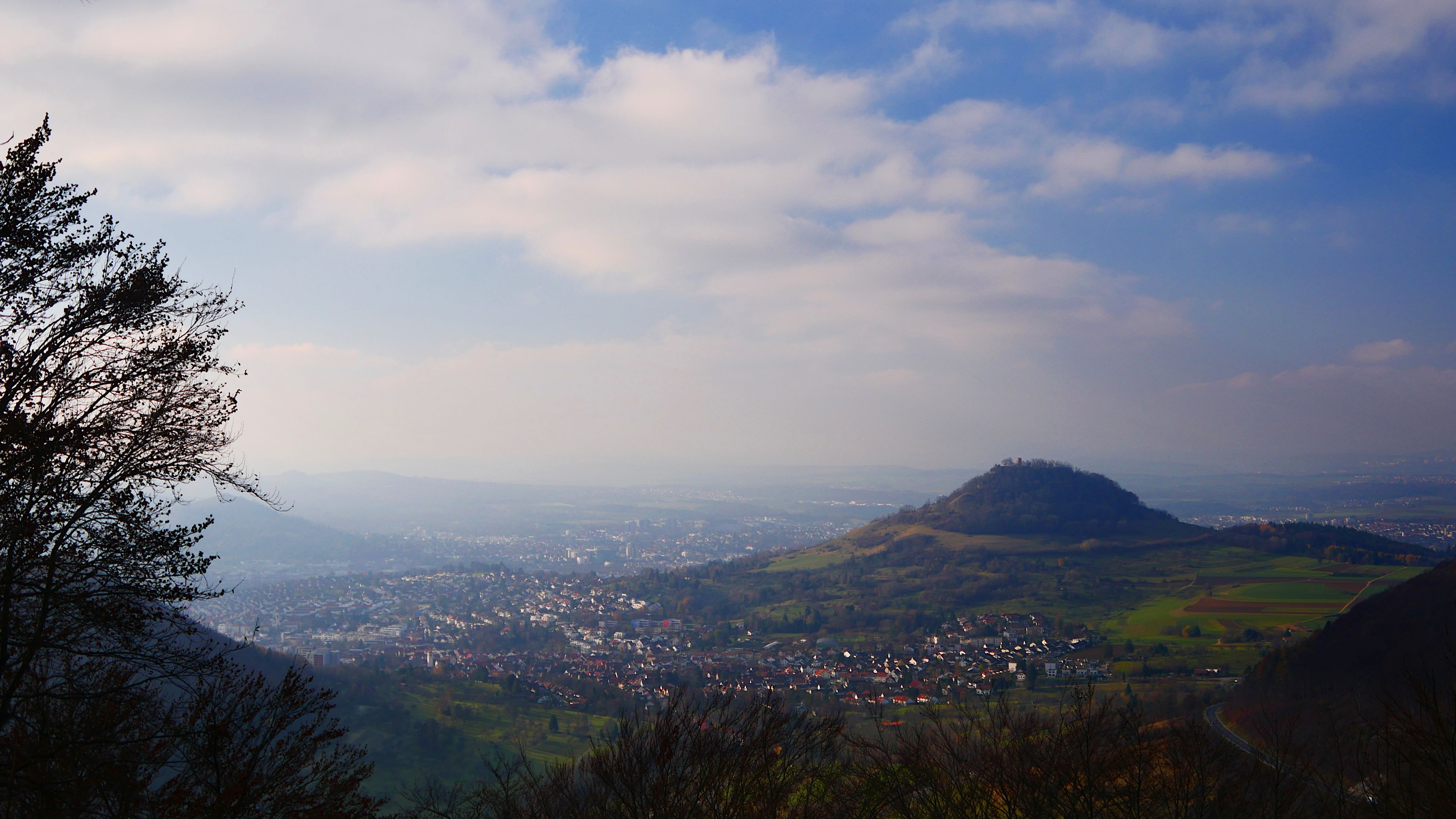 Une vue panoramique d’une ville nichée dans une vallée, avec une colline imposante en arrière-plan.