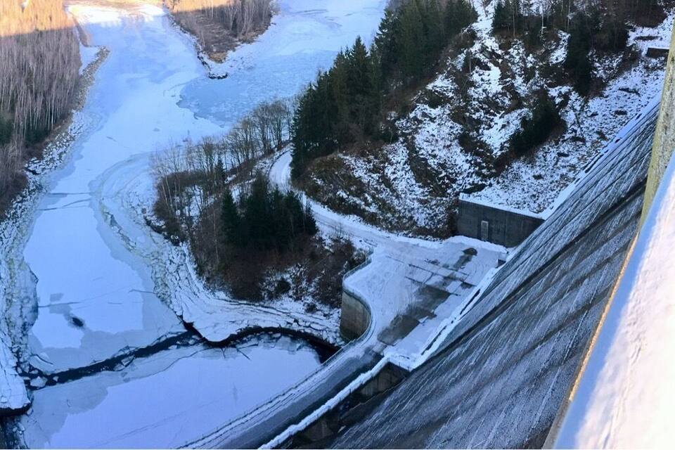 A snow-covered landscape with a winding road, a small building, and a river.