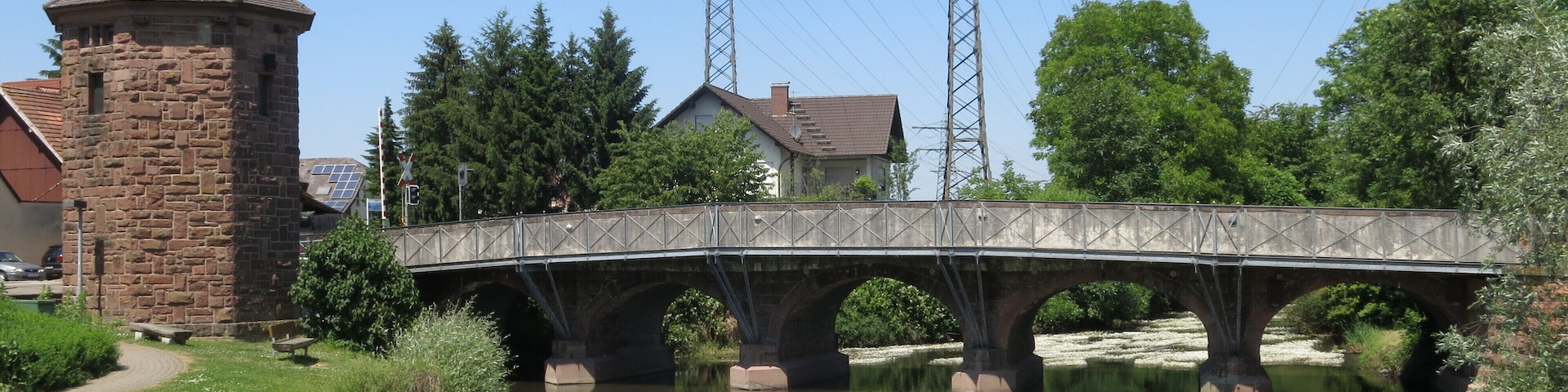 A stone bridge over a calm river, surrounded by greenery and a stone tower.