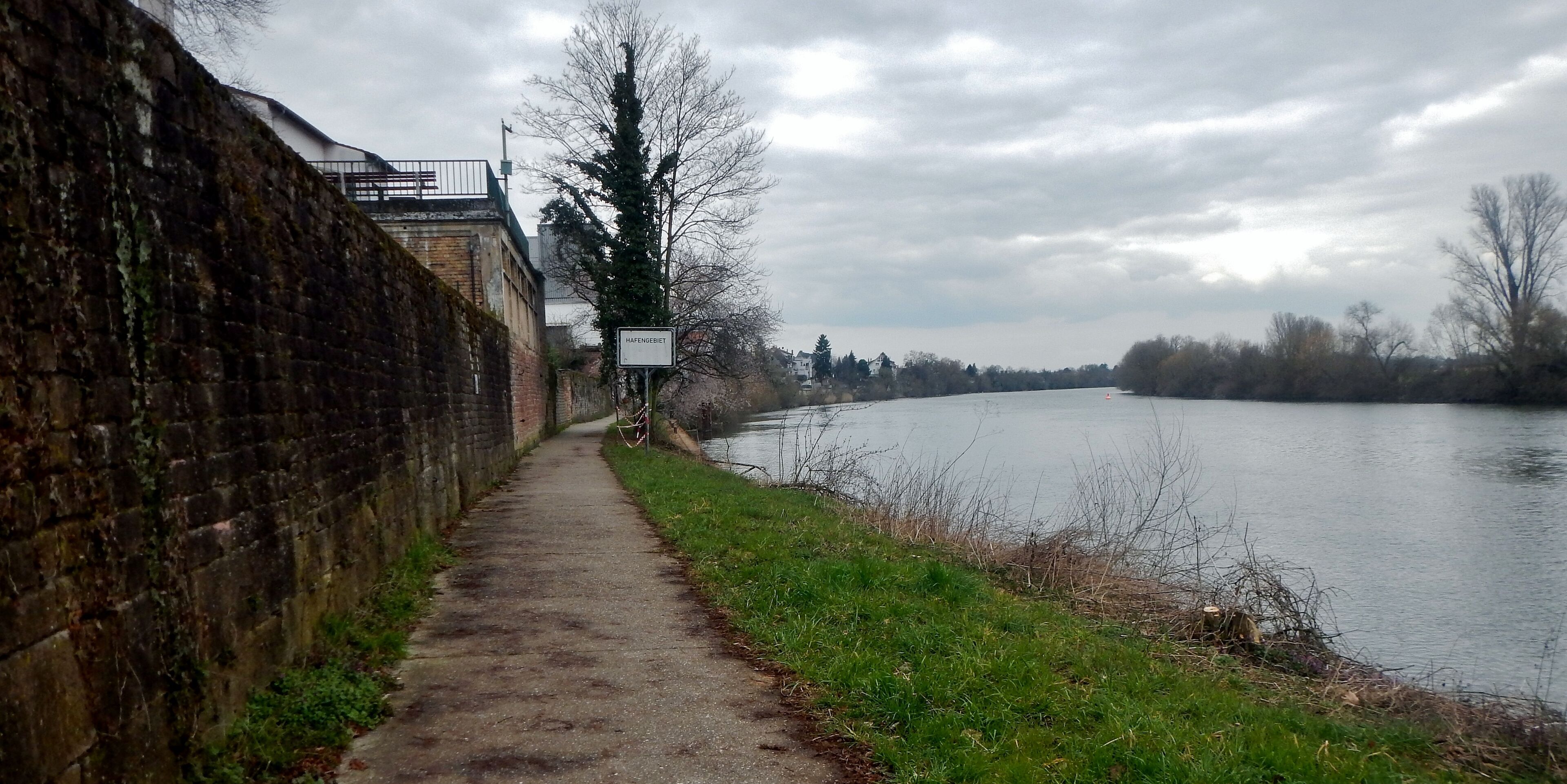A riverside path with a brick wall on one side and a sign that reads "HAFENGEBET".