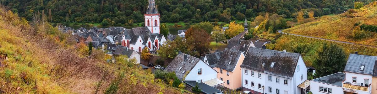 A village with a prominent church tower, surrounded by lush green hills and a river.