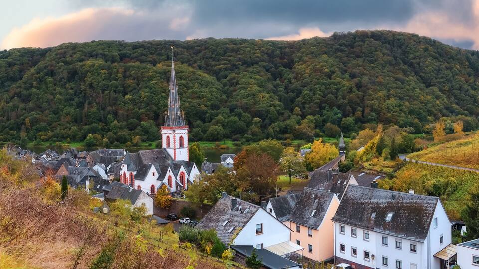 A village with a prominent church tower, surrounded by lush green hills and a river.