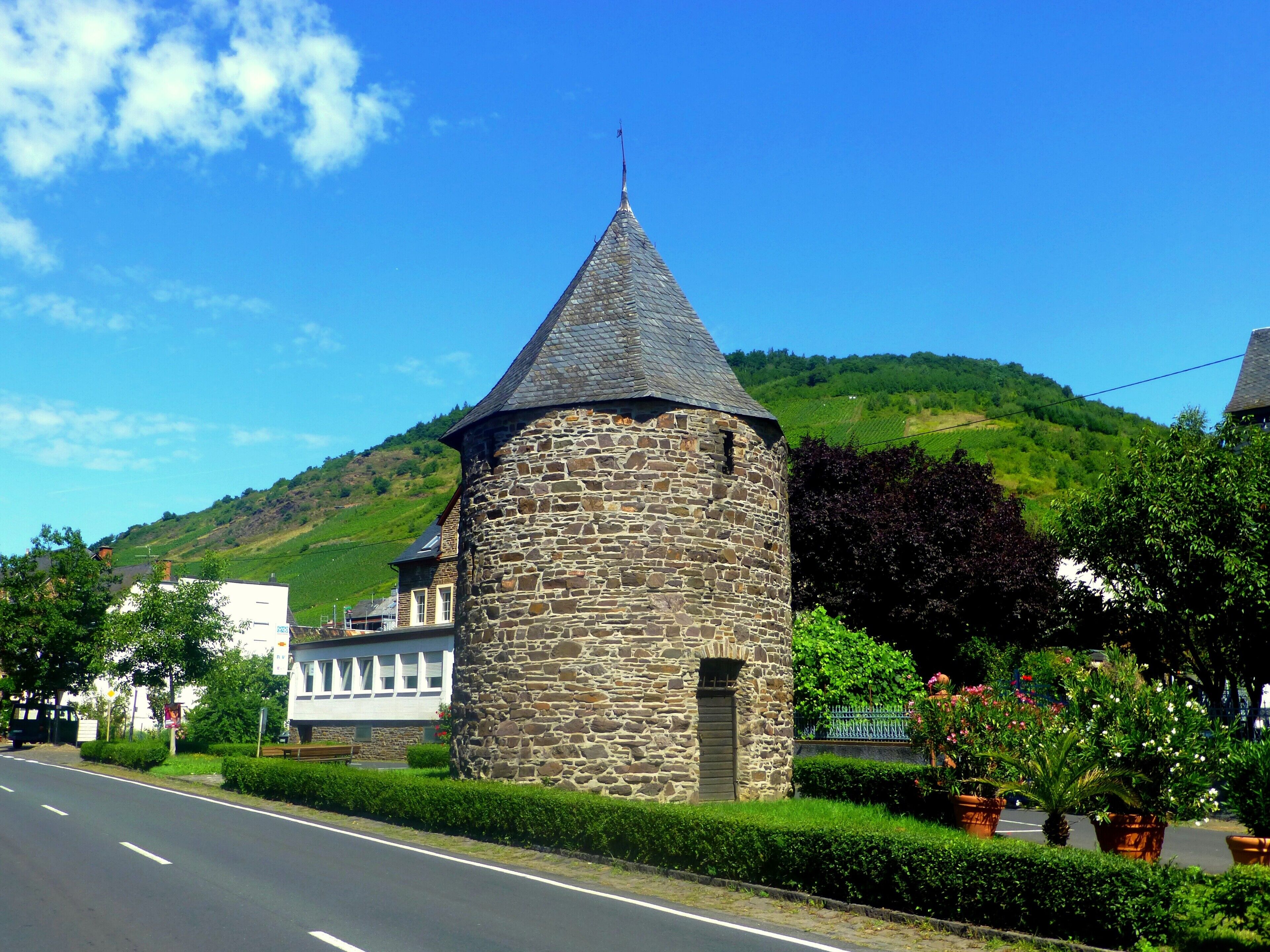 A stone tower with a conical roof, a road, and green hills in the background.