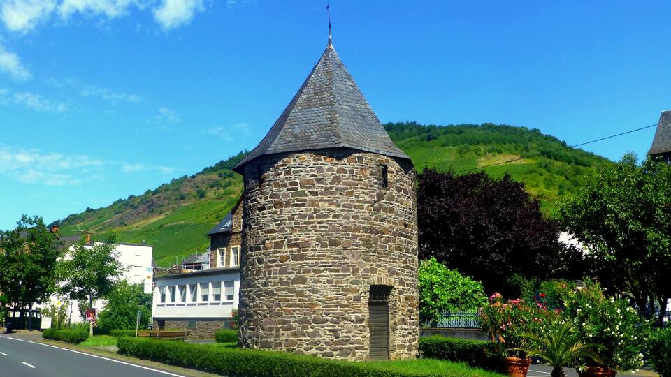 A stone tower with a conical roof, a road, and green hills in the background.
