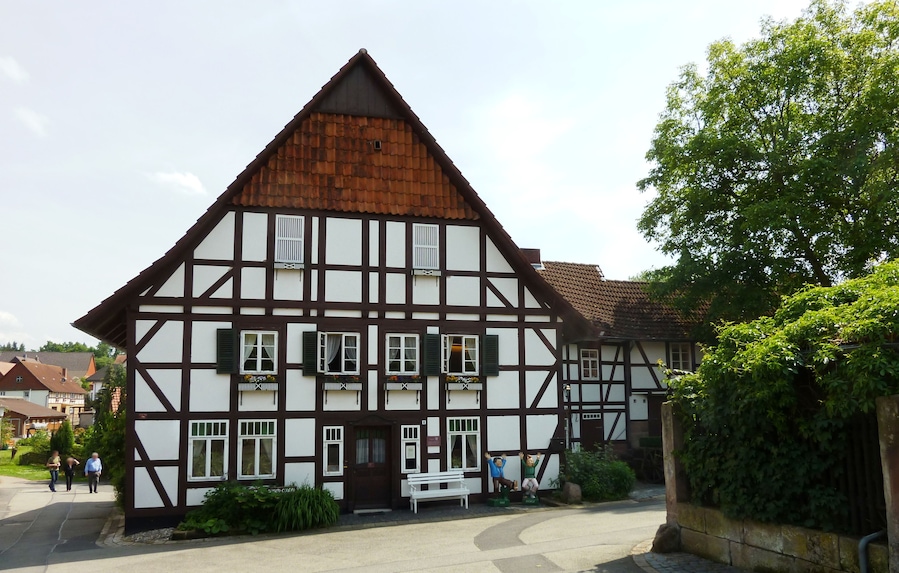 A traditional half-timbered house with a sloped roof, a bench, and a small garden area.