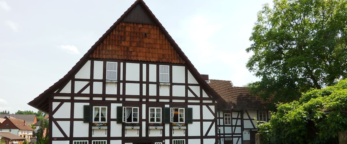 A traditional half-timbered house with a sloped roof, a bench, and a small garden area.