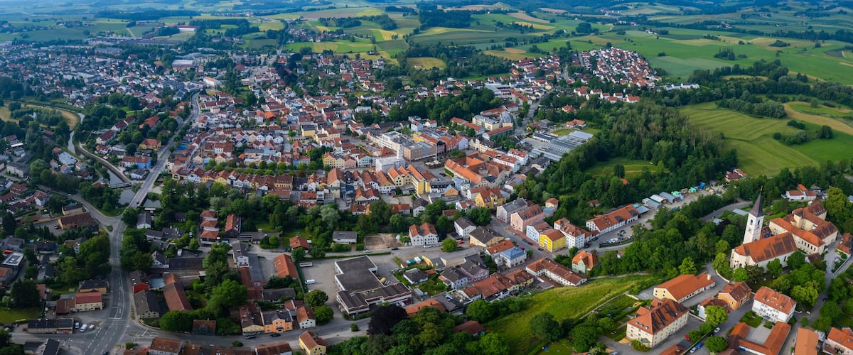 An aerial view of a town with a central square, surrounded by residential buildings and green fields.