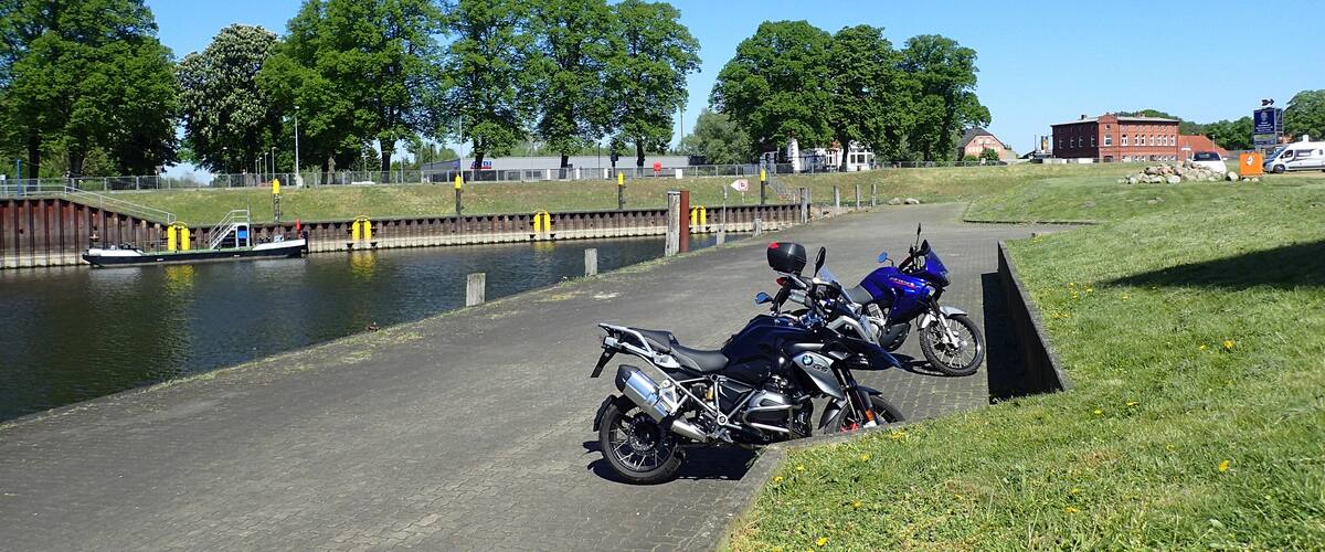 A canal with boats, a grassy area, and parked motorcycles.