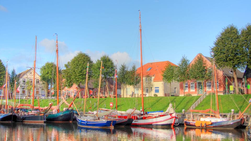 A harbor with several boats docked, a building with a red roof, and a grassy embankment.