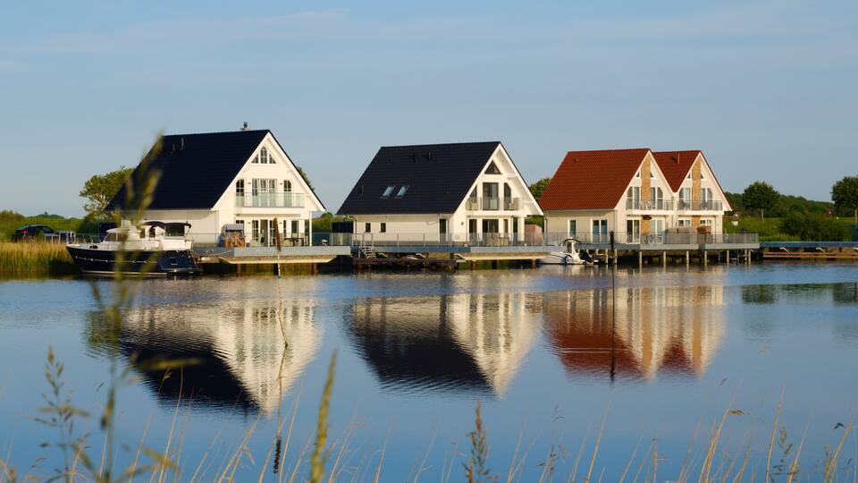 Three houses by a calm lake with reflections.