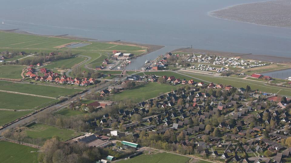 An aerial view of a coastal town with a river, green fields, and residential areas.