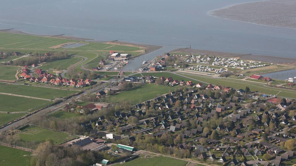 An aerial view of a coastal village with houses, fields, and a body of water.