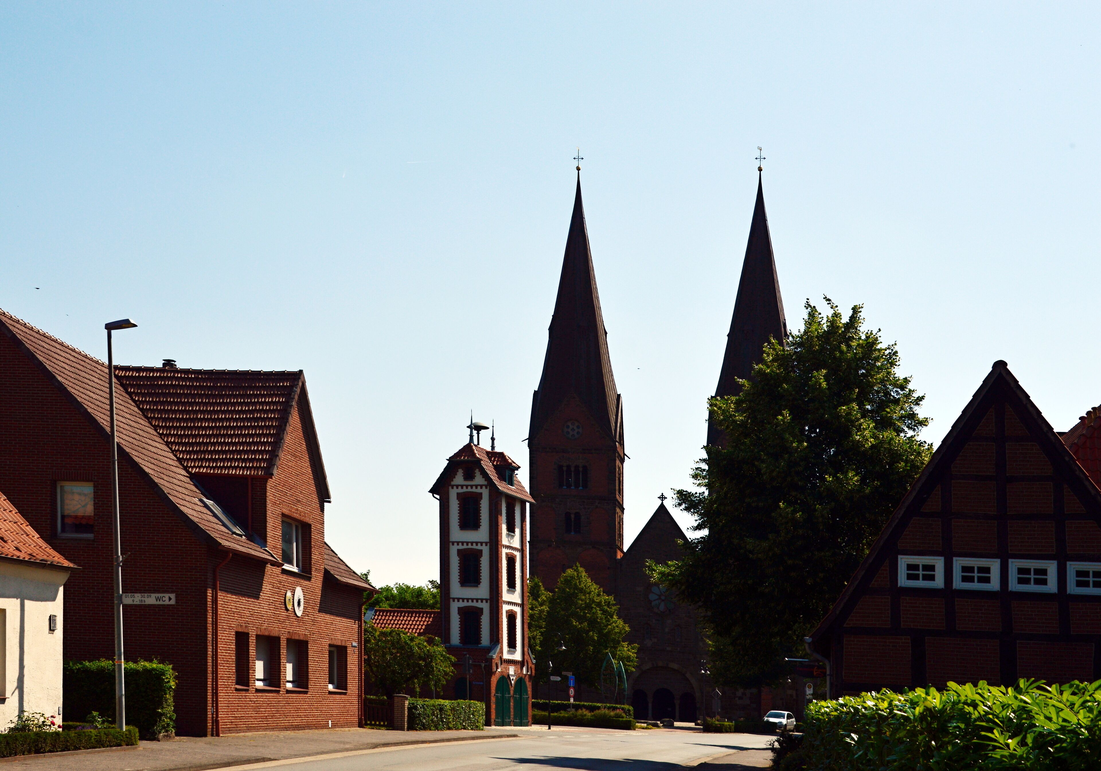 A church with two tall spires, a bell tower, and traditional half-timbered houses.