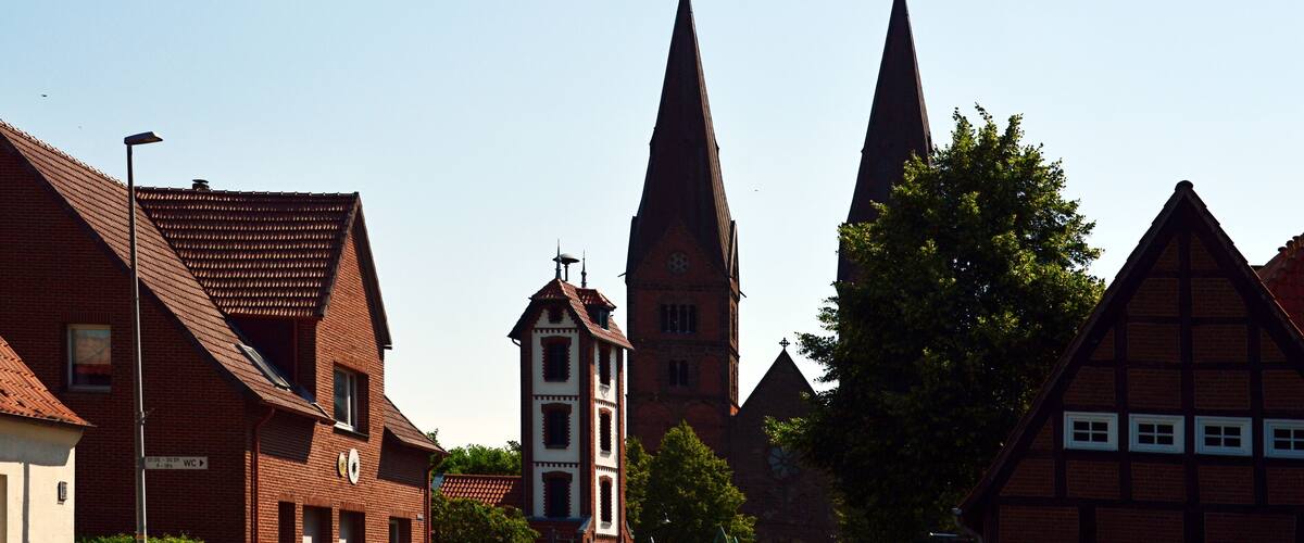 A church with two tall spires, a bell tower, and traditional half-timbered houses.