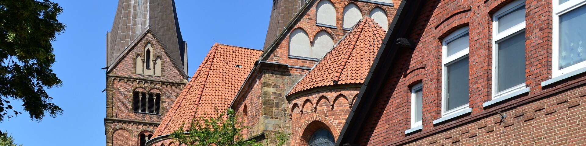 Una iglesia histórica con altas agujas y techo de tejas rojas, rodeada de edificios de ladrillo tradicionales.