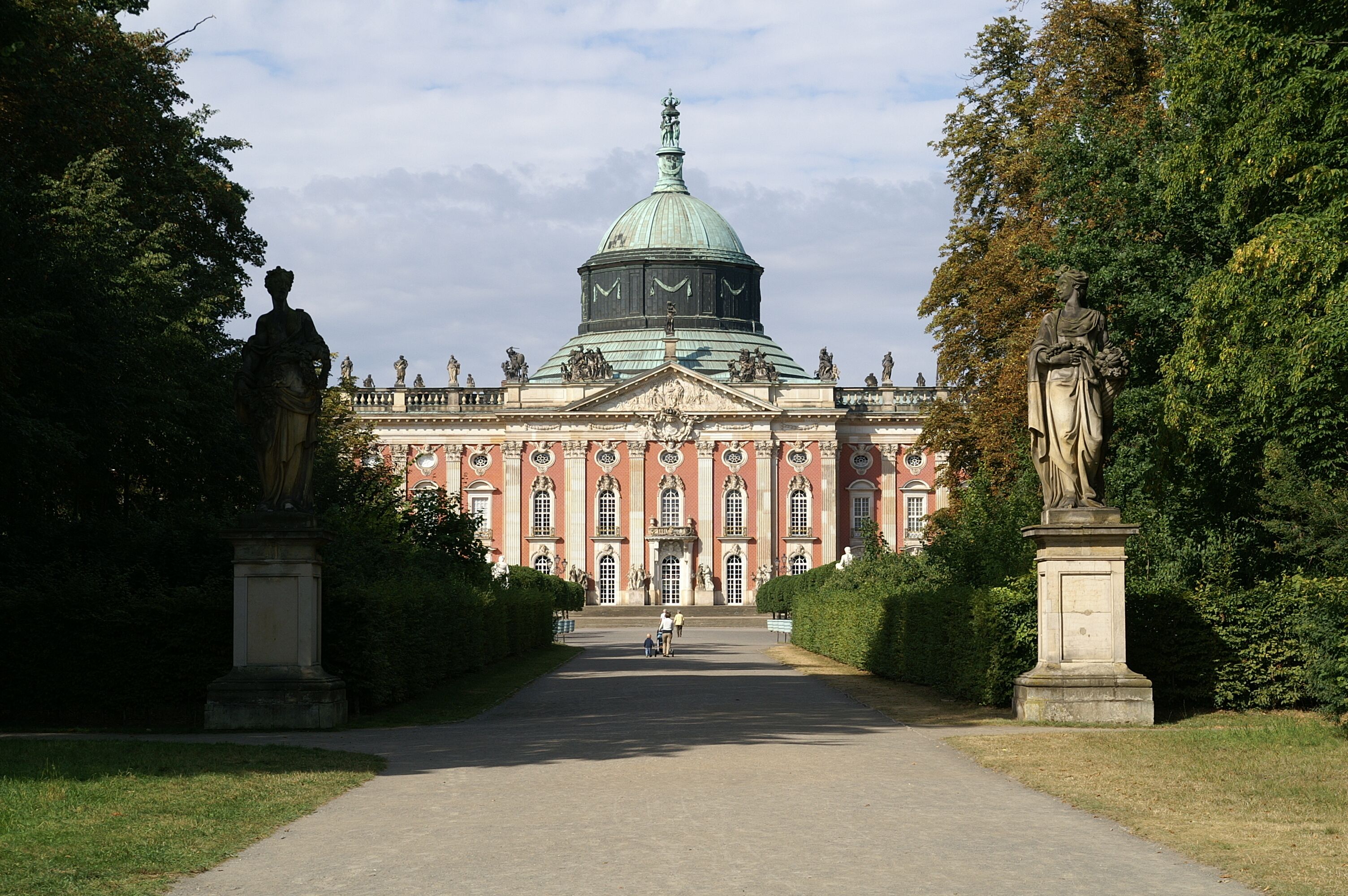 A grand building with a large dome and statues in a formal garden setting.