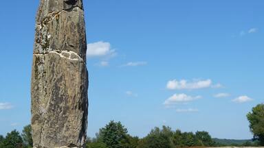 A tall standing stone in a grassy field with a clear blue sky.