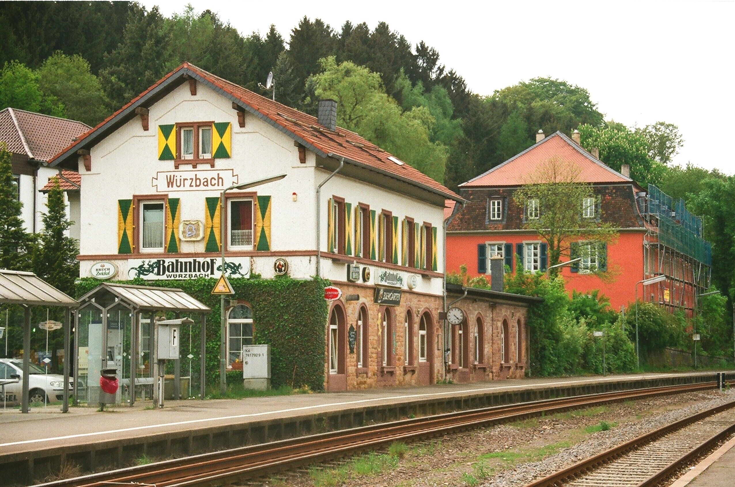 A train station with a white building labeled 'Würzbach' and a red building in the background.