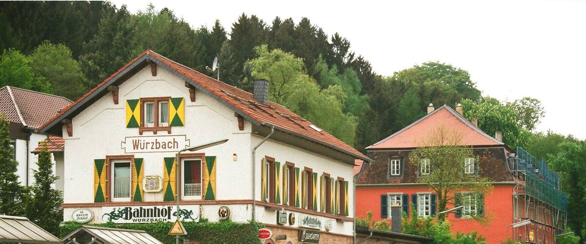 A train station with a white building labeled 'Würzbach' and a red building in the background.