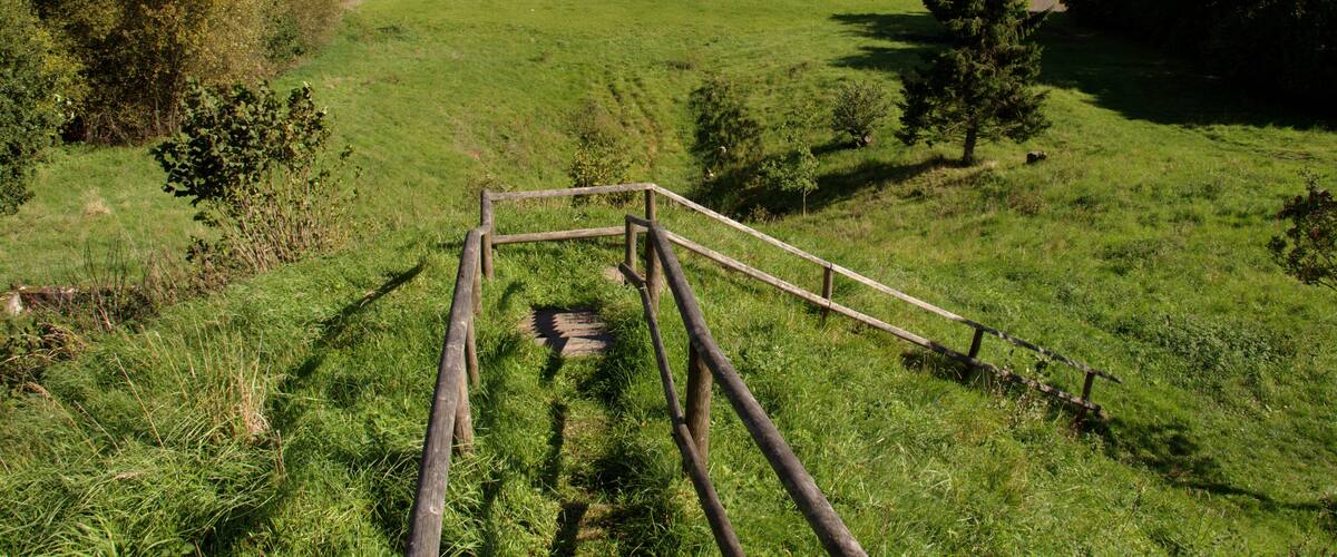 A grassy field with a wooden structure in the foreground and a distant village.