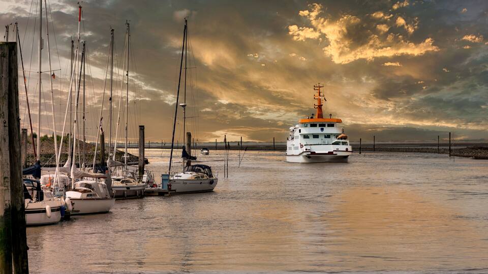 A harbor with multiple sailboats docked, a large white vessel with an orange top, and a dramatic sky with clouds.