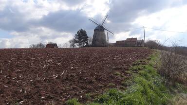 A windmill on a hill with a cloudy sky.