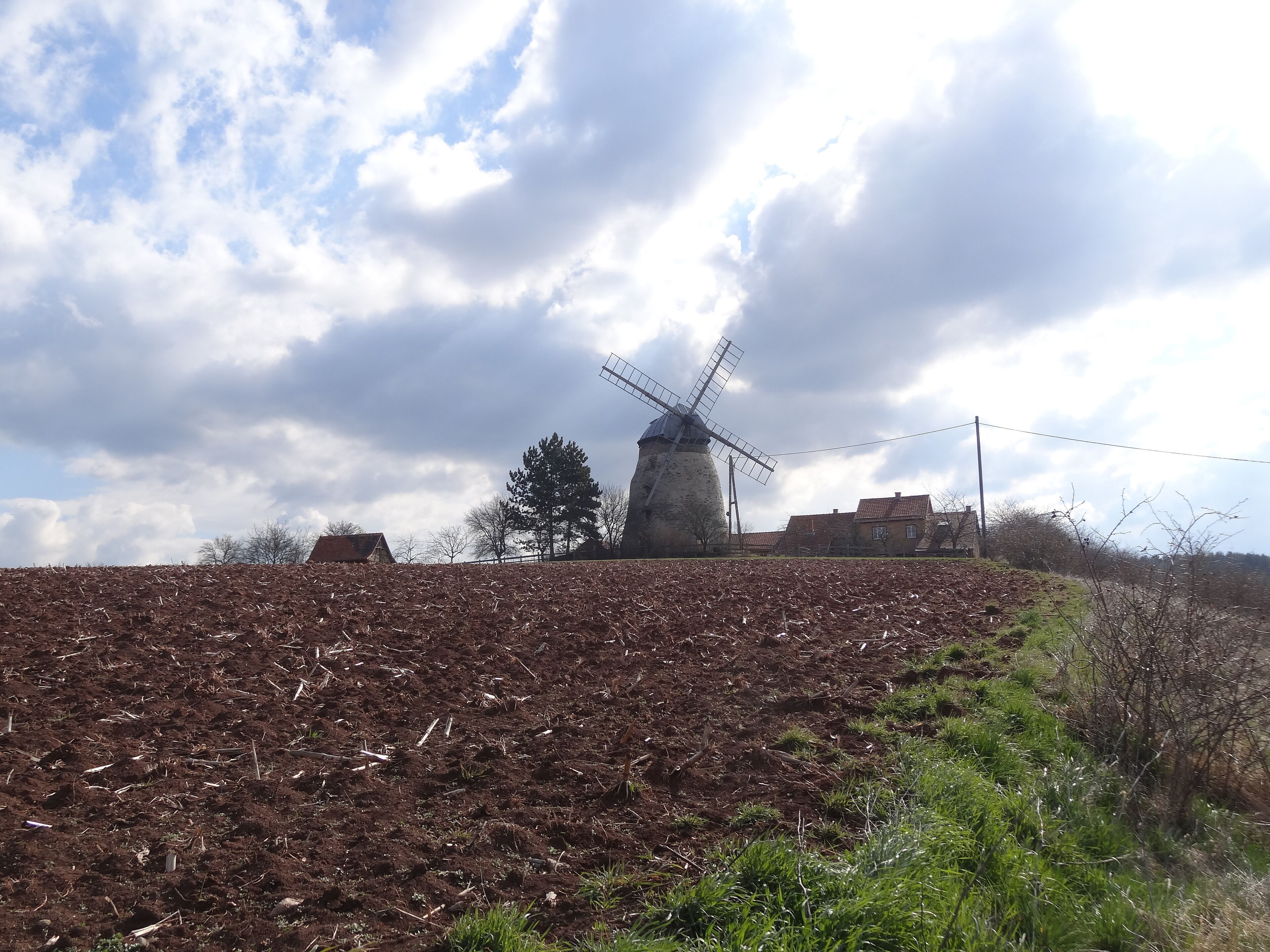 A windmill on a hill with a cloudy sky.