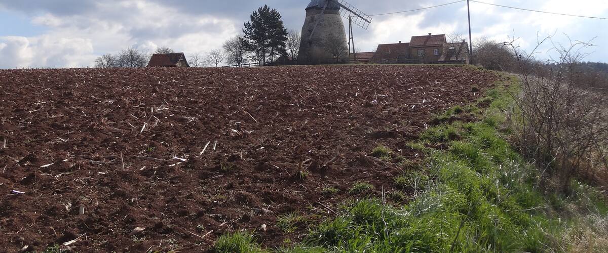 A windmill on a hill with a cloudy sky.