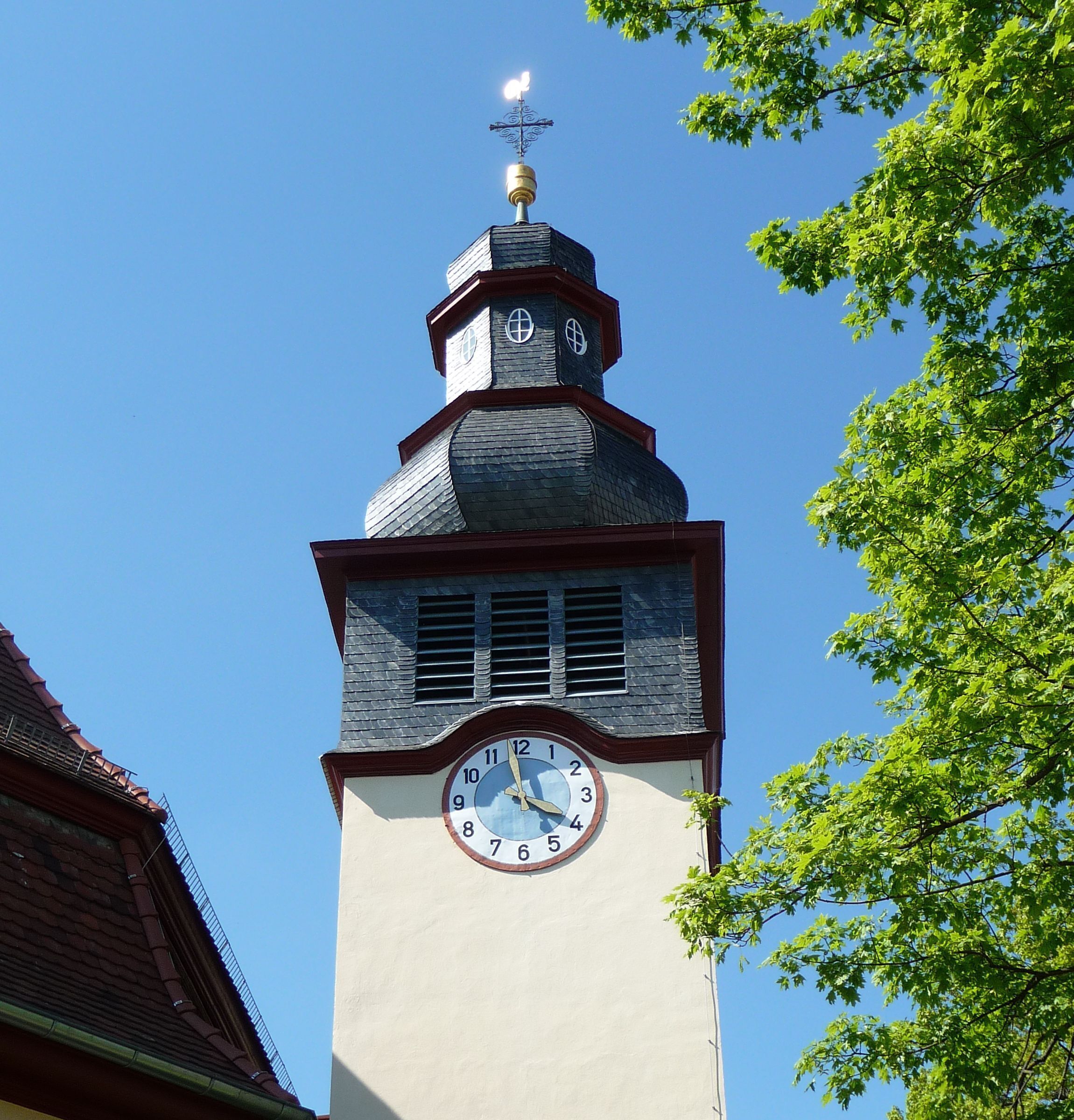 A church tower with a clock, a weather vane, and a cross on top.