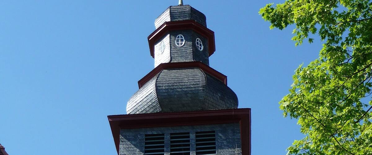 A church tower with a clock, a weather vane, and a cross on top.