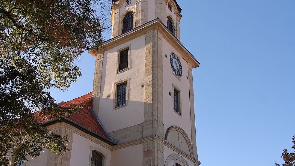 A historic church with a clock tower, surrounded by autumn trees and parked cars.