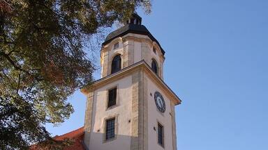 Uma igreja histórica com torre do relógio, rodeada por árvores de outono e carros estacionados.