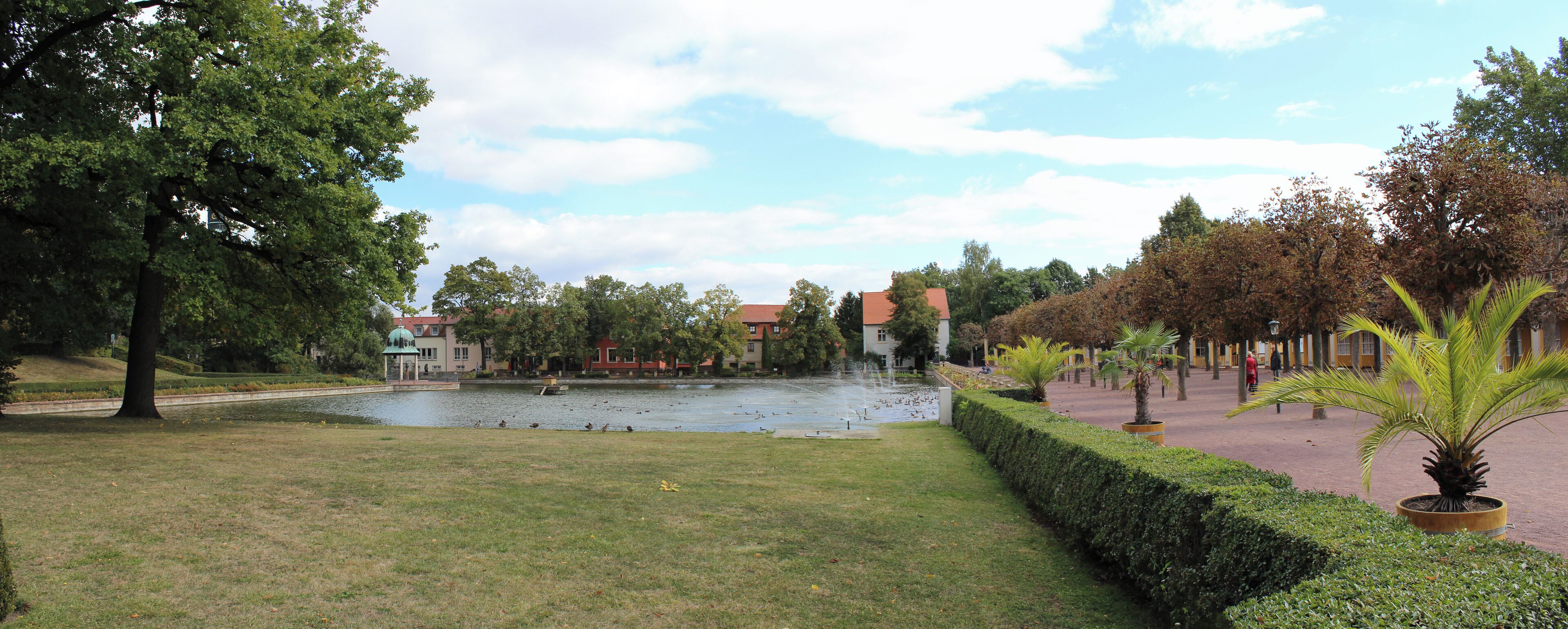 A park with a pond, trees, and buildings in the background.