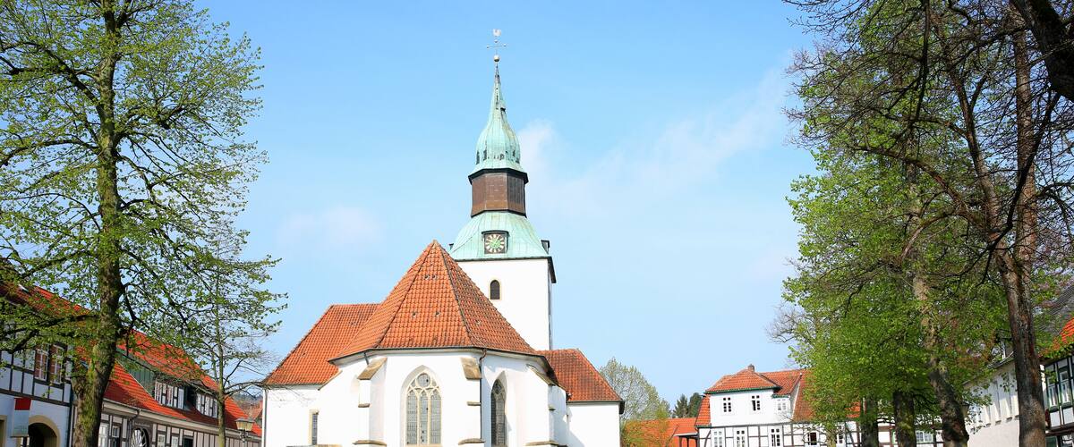 A church with a red roof and a green spire, surrounded by cobblestone streets and traditional buildings.